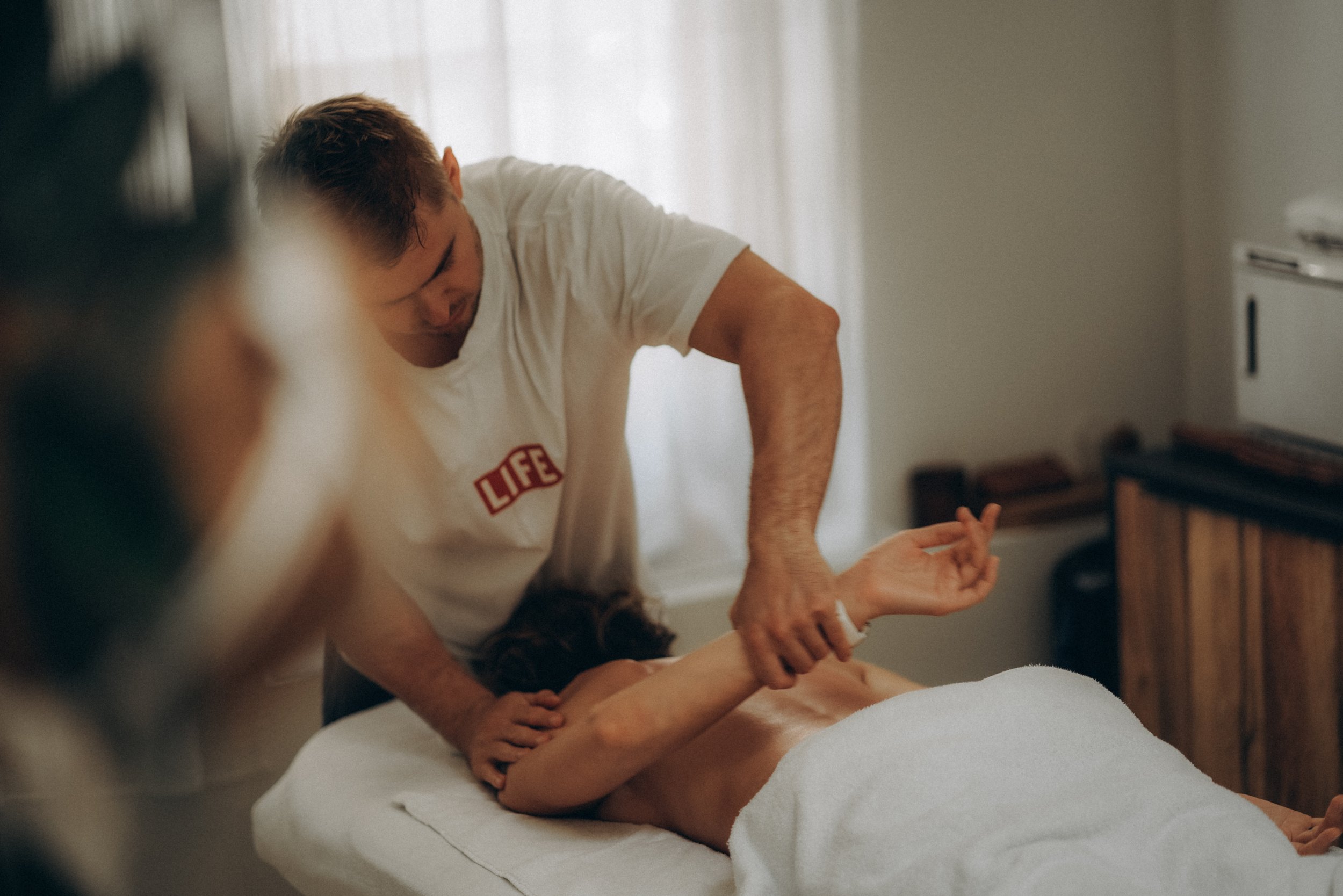 A man giving a massage to a woman lying on a massage table in a room with soft lighting.